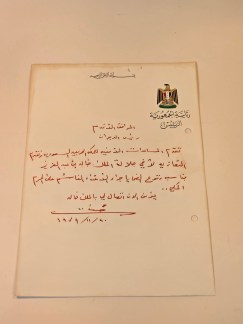 A close-up of a handwritten letter in Arabic, signed by Saddam Hussein, with an Egyptian government emblem at the top. The letter is authenticated by AutographCOA.