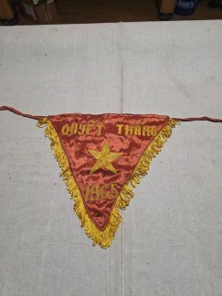 A red, satin-like pennant with a yellow star and embroidered text. The words "QUYET THANG" and "1965" are clearly visible.