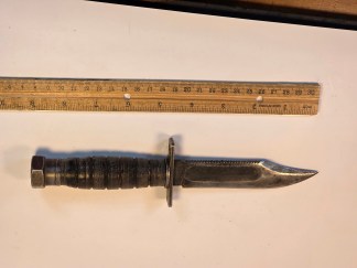 A Camillus pilot survival knife with a leather handle and a clip-point blade. The knife is shown with its original leather sheath that has a front pouch.