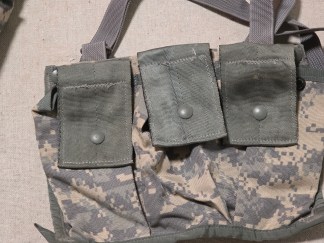 Group shot of a UCP FLC vest, a folded Coyote Brown neck gaiter, and a pile of military-grade grey plastic buckles.