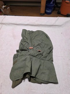 Front and interior view of a US Army M-65 Field Jacket hood showing the OD green fabric, drawstring toggles, and the warm, thick fleece lining