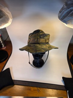 Front view of a Vietnam War-era Tiger Stripe camouflage boonie hat displayed on a black stand.
