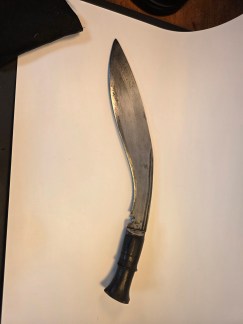 Close-up of an antique 17-inch Gurkha Kukri fighting knife showing the curved blade, dark wood handle, and patina.