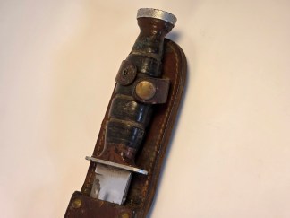 Vintage US Military fighting knife with a stacked leather handle and polished 5.5-inch blade, shown next to its original brown leather sheath.