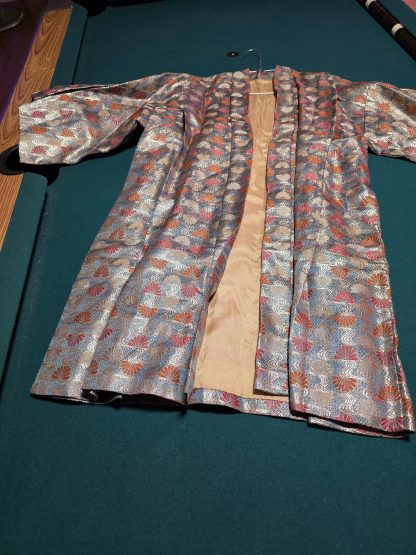 Close-up of metallic brocade fabric on a WWII era child's kimono showing fan and wave patterns in gold silver blue and red