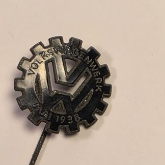 (Alt Text): Metal stickpin featuring a gear-shaped logo with "VOLKSWAGENWERK MAI 1938" and the VW monogram.